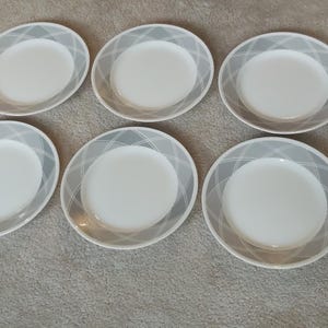 Puede incluir: Un conjunto de diez platos ovalados blancos con un patrón geométrico gris en el borde. Los platos están dispuestos sobre una superficie de color neutro, ideales para una presentación elegante.