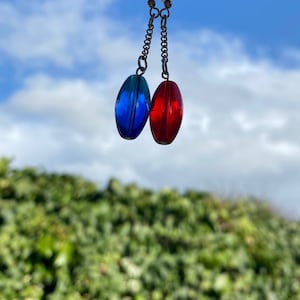 May include: A pair of dangle earrings with blue and red glass beads. The earrings are hanging against a blue sky with white clouds.
