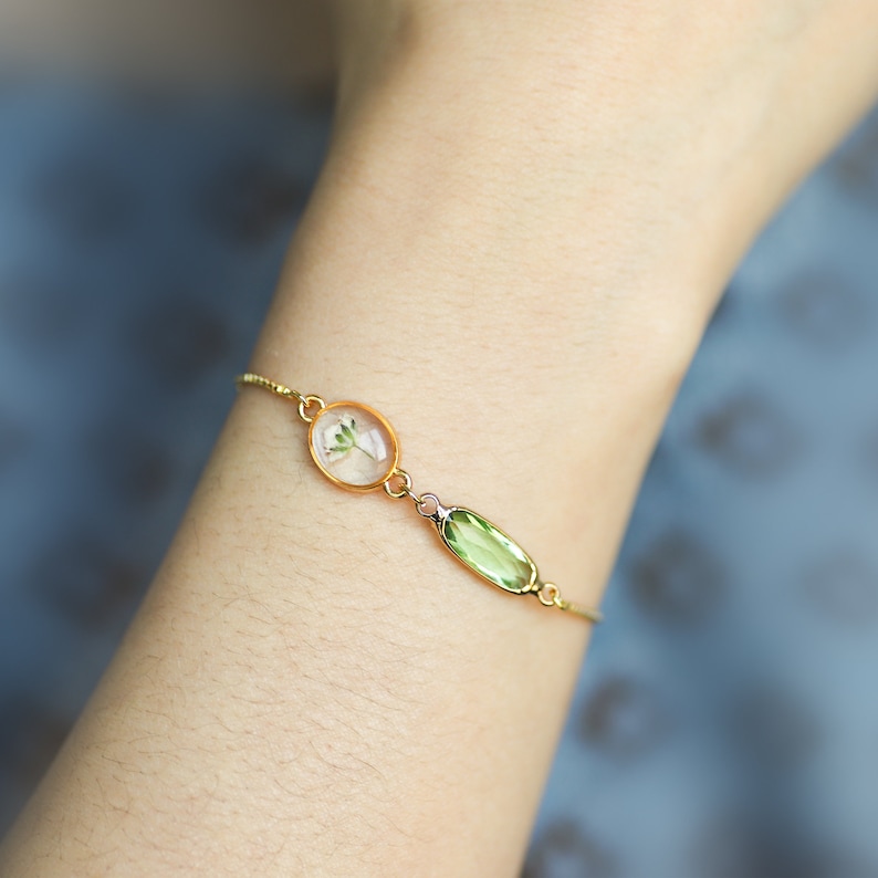 May include: A gold chain bracelet with a delicate pressed flower and a green oval gemstone charm.