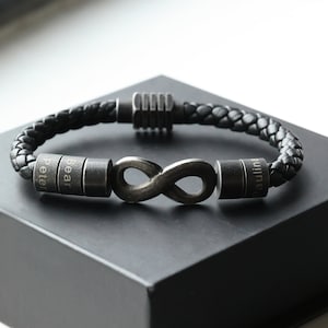 Puede incluir: Pulsera de cuero negro con un dije de símbolo de infinito y tres cuentas de metal grabadas que dicen "Peter", "Bear" y "Paulina".