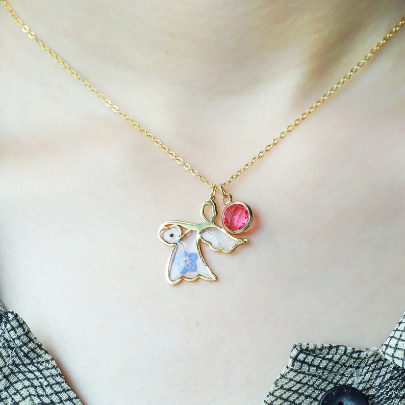 May include: A gold chain necklace with a delicate angel pendant featuring a pressed flower design and a pink crystal charm.