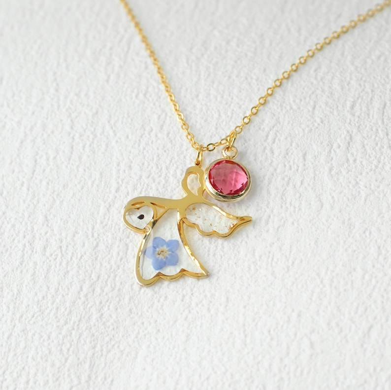 May include: Gold necklace with a delicate angel pendant featuring a blue flower and a pink gemstone.