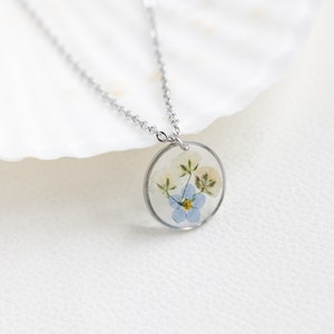 May include: A silver chain necklace with a round pendant featuring pressed blue and white flowers encased in clear resin.