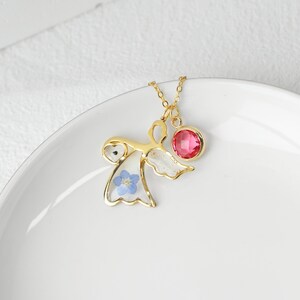 May include: Gold necklace with a delicate angel pendant featuring a pressed blue flower and a pink gemstone.
