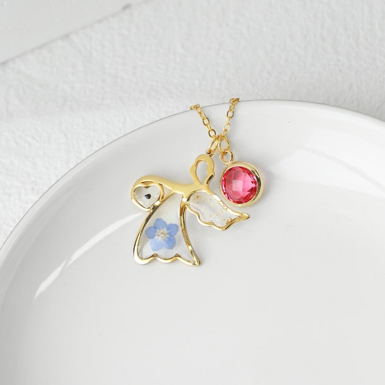 May include: Gold necklace with a delicate angel pendant featuring a pressed blue flower and a pink gemstone.