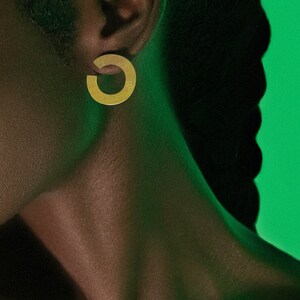 May include: A close-up of a person's ear wearing a gold hoop earring. The earring is a simple, circular design with a smooth, polished finish.