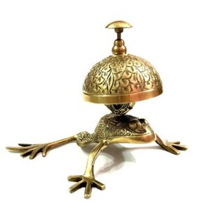 Pode incluir: Uma figura de sapo de ouro com um sino decorativo nas costas. O sino tem um design floral e um pequeno bot&atilde;o no topo.
