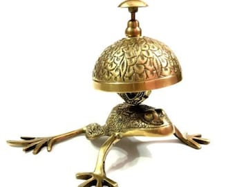 May include: A gold frog figurine with a decorative bell on its back. The bell has a floral design and a small knob on top.