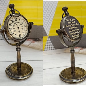 May include: A brass compass clock with a white face and black numbers. The clock is on a stand with a decorative base. The back of the clock is engraved with the text "It's all your time now! Always know what a difference you have made. Heartland ILC Retirement 12/30/2012".