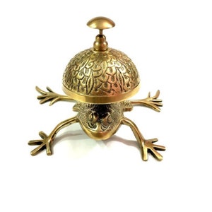 Pode incluir: Um sino de servi&ccedil;o em forma de sapo dourado com uma c&uacute;pula decorativa com padr&otilde;es. O sino &eacute; feito de lat&atilde;o e tem um design tradicional.