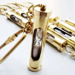 May include: A set of brass keychains with a small hourglass inside each. The keychains are attached to a gold chain with a lobster clasp.