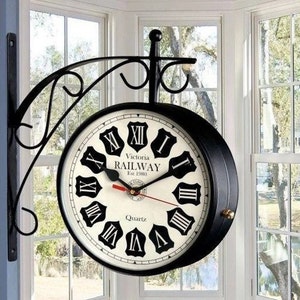 May include: Black double-sided clock with a white face and black Roman numeral hour markers. The clock face reads "Victoria Railway Est 1980" and "Quartz".
