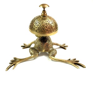 Pode incluir: Um sino de servi&ccedil;o dourado em forma de sapo com um topo decorativo e estampado. O sino &eacute; feito de metal e tem um design tradicional.