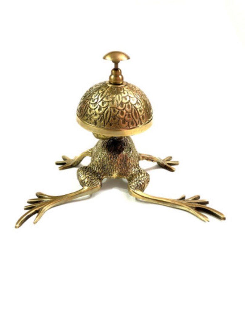 Pode incluir: Um sino de servi&ccedil;o dourado em forma de sapo com um topo decorativo e estampado. O sino &eacute; feito de metal e tem um design tradicional.