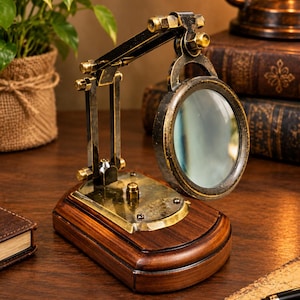 May include: A magnifying glass mounted on an adjustable brass and dark metal arm, attached to a polished wooden base. A small brass plaque on the base features engraved text that reads "Dollond London". The lens is circular with a metallic frame.