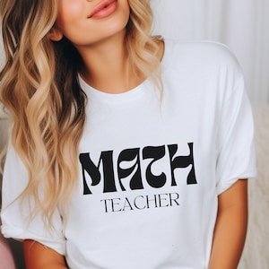 May include: White t-shirt with black text that reads "MATH TEACHER" in a retro font.