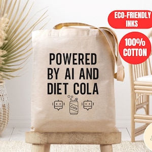 May include: A beige tote bag with black text that reads "Powered by AI and Diet Cola". The bag has a black and white illustration of a can of cola and a robot. The bag is made of 100% cotton and uses eco-friendly inks.