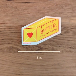 May include: A yellow stick of butter with a red heart and the text "BUTTER is my love language" on a white background. The sticker is 3 inches wide.