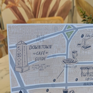 May include: A map titled "Downtown Cafe Guide" with illustrations of cafes and landmarks. The map includes the text "A local guide to the cafes & vibes in the city of 199 trees."