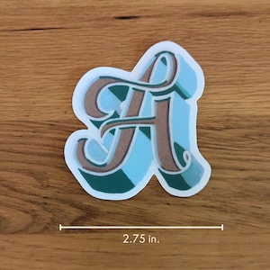 May include: A blue and green sticker with a brown stylized letter A. The sticker is 2.75 inches wide.