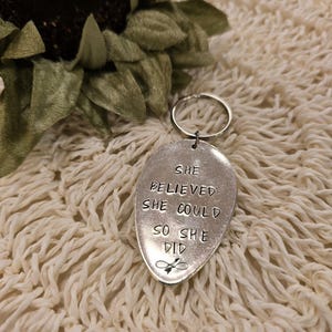 Puede incluir: Llavero de cuchara de plata con el texto "She believed she could so she did" y un pequeño símbolo de infinito.