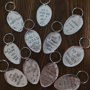 Puede incluir: Una colección de 11 llaveros de cuchara de plata con diferentes lemas grabados. Los lemas incluyen "Wild Heart Gypsy Soul", "Just a Small Town Girl", "You're My Favorite Asshole", "We Were Written in the Stars", "A Soul of a Mermaid Mouth of a Sailor", "The World is a Vampire", "Day Dreamer", "Don't Do Stupid Shit Love Mom", "Hey I Heard You Are a Wild One", "Mama Tried", y "amBITCHous".