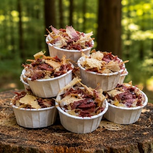 May include: A pyramid stack of six white paper cups filled with a mixture of dark red dried meat pieces and light tan wood shavings. The cups are arranged in a tiered formation, showcasing the textured contents of each individual container.