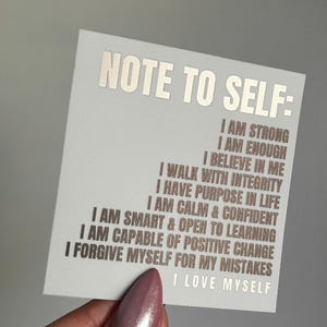 Pu&ograve; includere: Un biglietto bianco con il testo "NOTE TO SELF:" stampato in lamina argentata. Il biglietto presenta un elenco di affermazioni positive in lamina marrone, tra cui "Sono forte", "Sono abbastanza", "Credo in me", "Cammino con integrit&agrave;", "Ho uno scopo nella vita", "Sono calmo e sicuro", "Sono intelligente e aperto all'apprendimento", "Sono capace di un cambiamento positivo", "Mi perdono i miei errori", e "Mi amo".