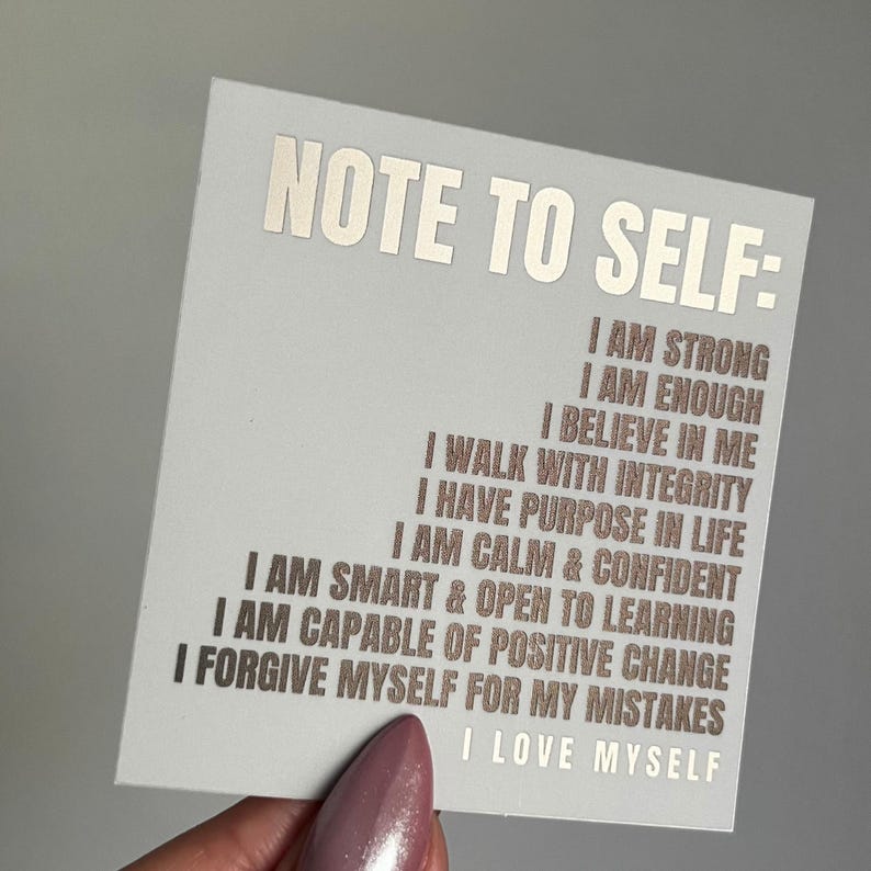 Pu&ograve; includere: Un biglietto bianco con il testo "NOTE TO SELF:" stampato in lamina argentata. Il biglietto presenta un elenco di affermazioni positive in lamina marrone, tra cui "Sono forte", "Sono abbastanza", "Credo in me", "Cammino con integrit&agrave;", "Ho uno scopo nella vita", "Sono calmo e sicuro", "Sono intelligente e aperto all'apprendimento", "Sono capace di un cambiamento positivo", "Mi perdono i miei errori", e "Mi amo".