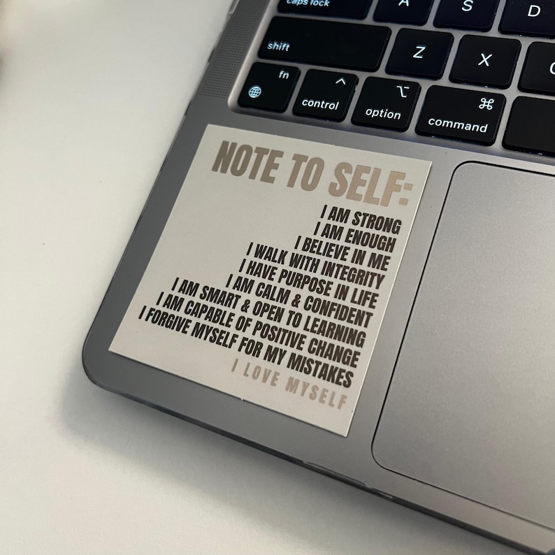 Pu&ograve; includere: Un adesivo beige con il testo "Note to Self:" e un elenco di affermazioni positive in testo nero. L'adesivo &egrave; su un laptop argentato.