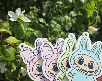 May include: A collection of colorful bunny-shaped keychains. Each keychain features a cartoon bunny design with a large bow or hood, and a wide, toothy grin. The keychains are in shades of pink, green, and blue.