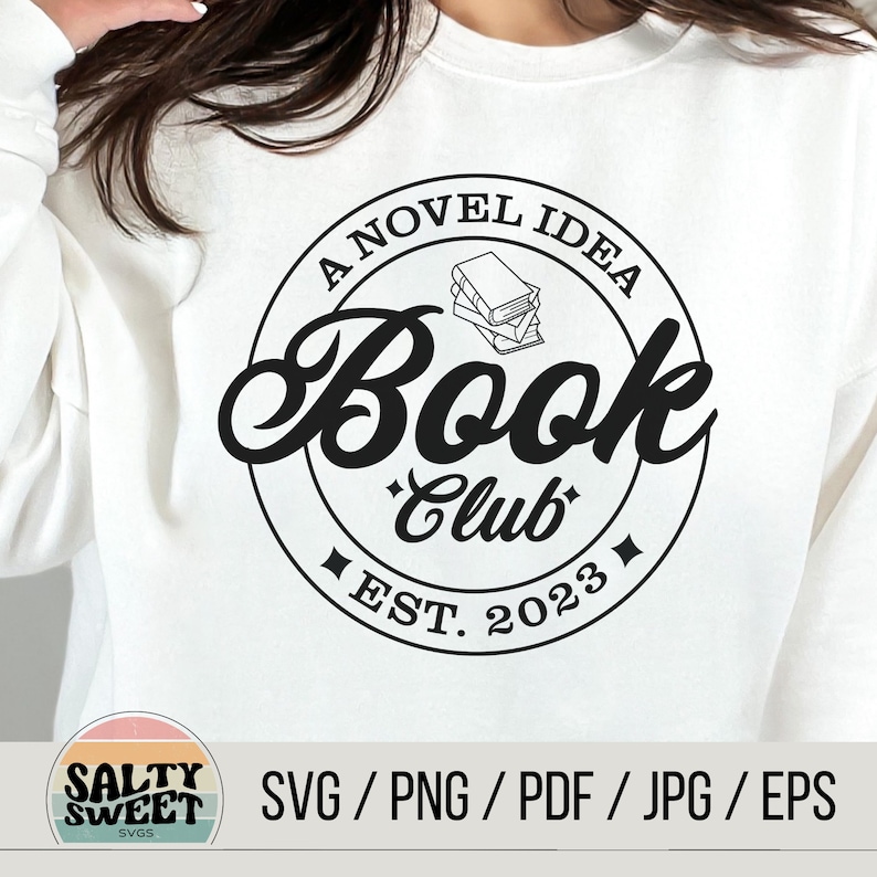 K&ouml;nnte beinhalten: Ein wei&szlig;es Sweatshirt mit einem schwarzen Kreisdesign, auf dem "A Novel Idea Book Club Est. 2023" steht und sich eine Stapel B&uuml;cher im Kreis befindet.