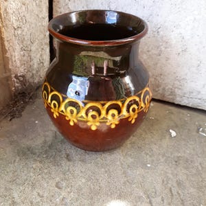 May include: A brown ceramic vase with a yellow and brown geometric design. The vase is round and has a wide mouth.