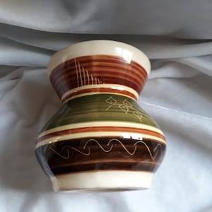 May include: A brown, green and white ceramic vase with a wide mouth and a narrow base. The vase has a striped pattern with a decorative design.