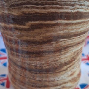 May include: A brown and white ceramic mug with a swirled pattern. The mug is sitting on a white fabric with a red, white and blue pattern.