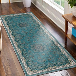 May include: A rectangular teal rug with an ornate floral pattern and a cream-colored border. The rug features a central medallion design and is placed on a dark wood floor. The rug is a decorative home decor item.