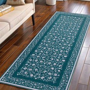 May include: Teal runner rug with a floral pattern. The rug features a central field of teal with a repeating white floral design. A white border frames the floral pattern, and the rug is placed on a hardwood floor.