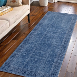 Könnte beinhalten: Ein langer, rechteckiger blauer Teppich mit einem Used-Look im Vintage-Stil. Der Teppich hat einen detaillierten floralen Rand und ein verblasstes, strukturiertes Aussehen. Er liegt auf einem Holzboden und verleiht dem Raum einen Hauch von Eleganz.