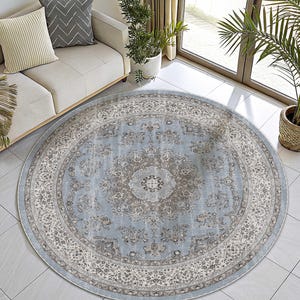 May include: A round area rug featuring a light blue central field with a detailed floral medallion in shades of gray and cream. The rug has a wide, intricate border with repeating floral patterns in muted tones of gray, white, and light blue.