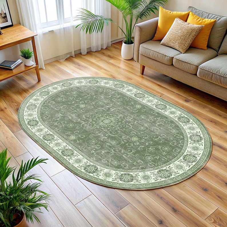 Pode incluir: Um tapete oval com um campo central verde-s&aacute;lvia e uma borda creme. O tapete apresenta um padr&atilde;o floral e de rolagem detalhado. Est&aacute; colocado sobre um piso de madeira em uma sala de estar. Dimens&otilde;es aproximadas: 200 cm x 300 cm.