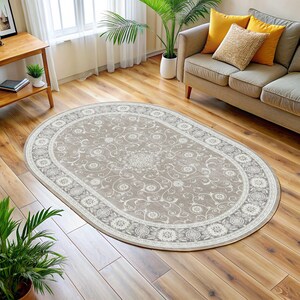May include: An oval area rug with a beige background and a detailed floral pattern. The rug has a white border with a repeating circular design. The rug is placed on a hardwood floor in a living room setting.