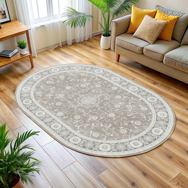 May include: An oval area rug with a beige background and a detailed floral pattern. The rug has a white border with a repeating circular design. The rug is placed on a hardwood floor in a living room setting.