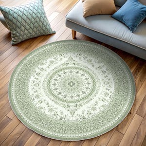 Può includere: Un tappeto rotondo con un intricato motivo floreale nei toni del verde e del bianco. Il tappeto presenta un design a medaglione centrale circondato da bordi dettagliati, creando un aspetto classico ed elegante. È posizionato su un pavimento in legno.