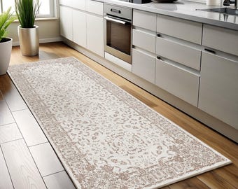May include: A white and beige patterned runner rug with a subtle floral design. The rug is placed in a kitchen with white cabinets and wood floors.