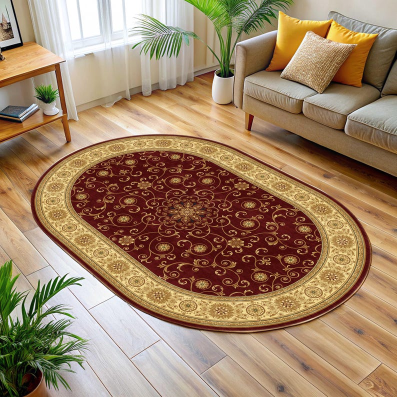 May include: Oval area rug with a burgundy field and a beige border. The rug features a detailed floral pattern in gold and beige. The rug is placed on a hardwood floor in a living room setting.