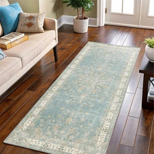 May include: A rectangular, light blue rug with an intricate floral pattern and a cream-colored border. The rug is placed on a dark wood floor, and is long and narrow, suitable for a hallway or entryway. The rug's design has a vintage or antique aesthetic.