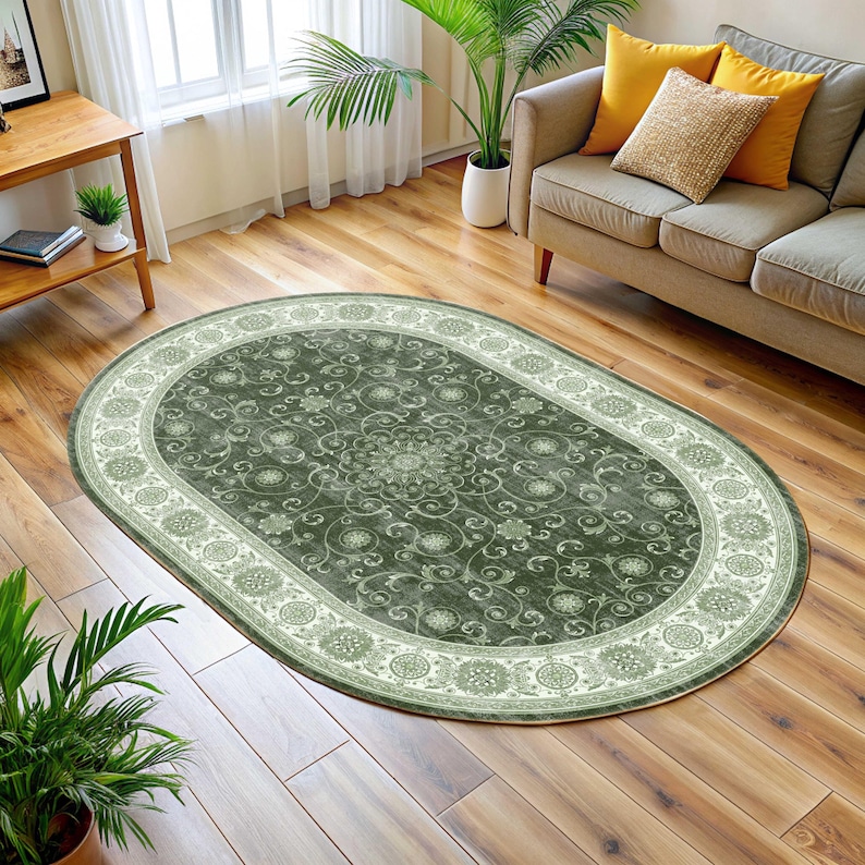 Pode incluir: Tapete oval com um centro verde escuro com um padr&atilde;o floral e uma borda verde clara. O tapete est&aacute; colocado sobre um piso de madeira, com um sof&aacute; e plantas ao fundo.