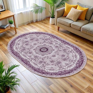 Puede incluir: Una alfombra ovalada con un patrón floral en tonos de morado y crema. La alfombra tiene un borde detallado y un medallón central.