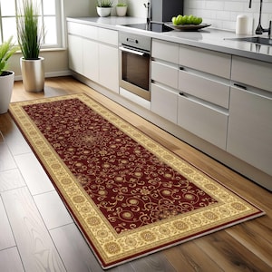 Könnte beinhalten: Ein rechteckiger Läufer mit einer tiefroten Mitte, die mit einem sich wiederholenden goldenen Blumen- und Rankenmuster verziert ist. Der Teppich ist von einer breiten, verzierten Bordüre in Creme- und Goldtönen umrahmt, die kreisförmige Motive zeigt.