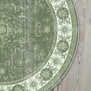 May include: A round, sage green rug with an ornate floral design. The rug features a central medallion and a decorative border with repeating floral patterns in shades of green and white. The rug's design includes swirling vines and floral motifs.